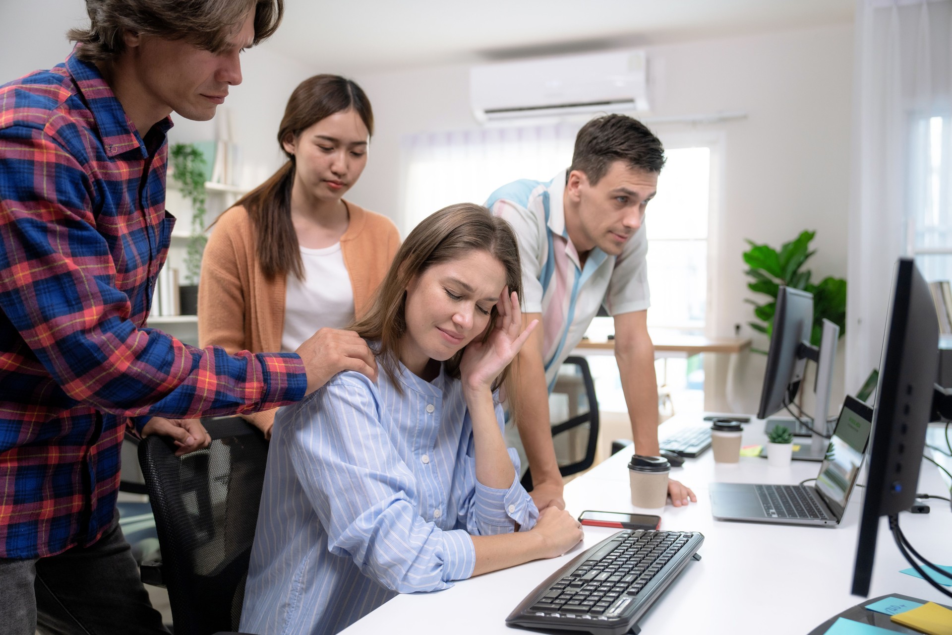 Group of colleagues comforting an unhappy female colleague in the office.