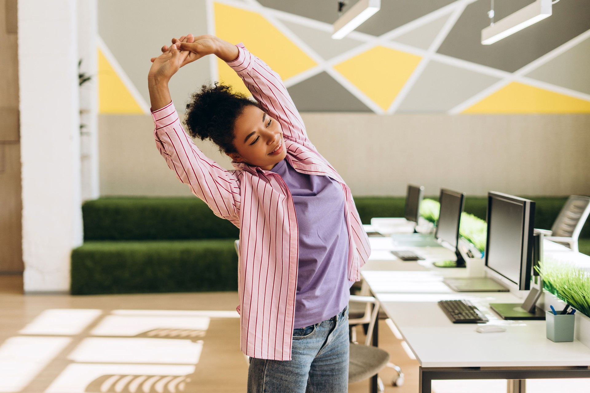 Smiling African American manager stretching arms at workplace in modern office